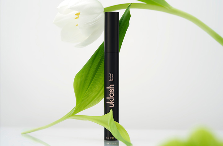 UKLASH Eyelash Serum in front of a white lily