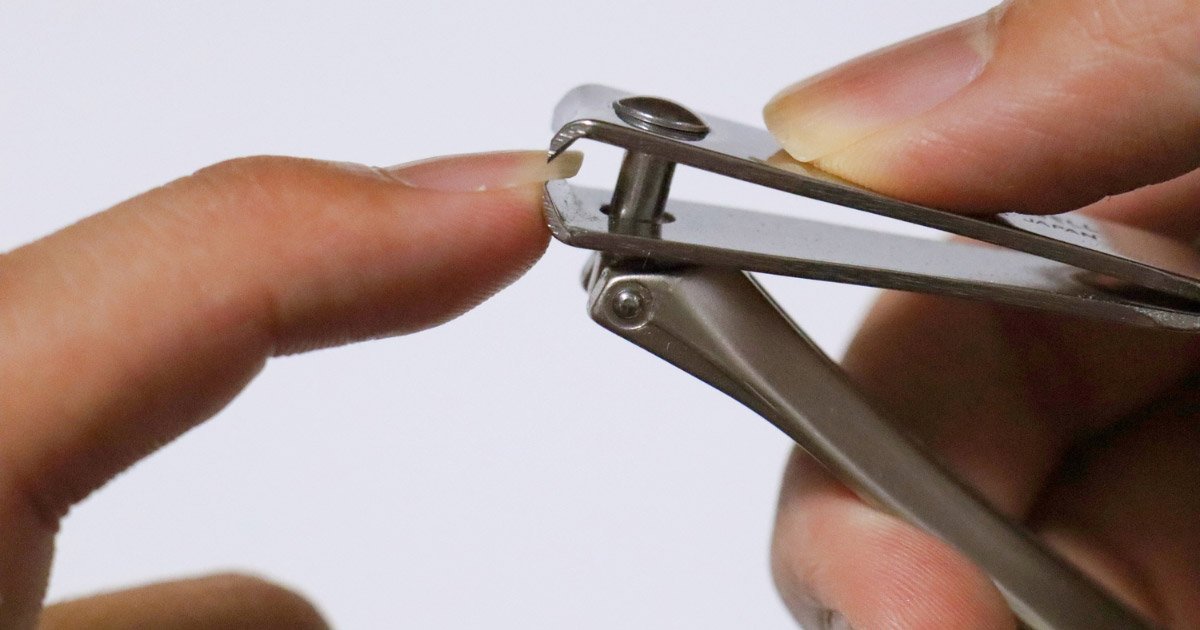 A close-up of a person using silver metal clippers to trim a fingernail.