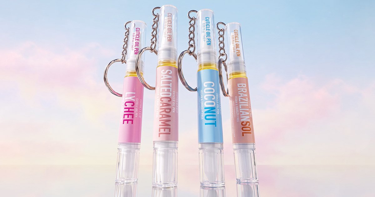 Four cuticle oil keychain pens lined up vertically against a pastel pink and blue-sky background, labelled from left to right: Lychee, Salted Caramel, Coconut, and Brazilian Sol.